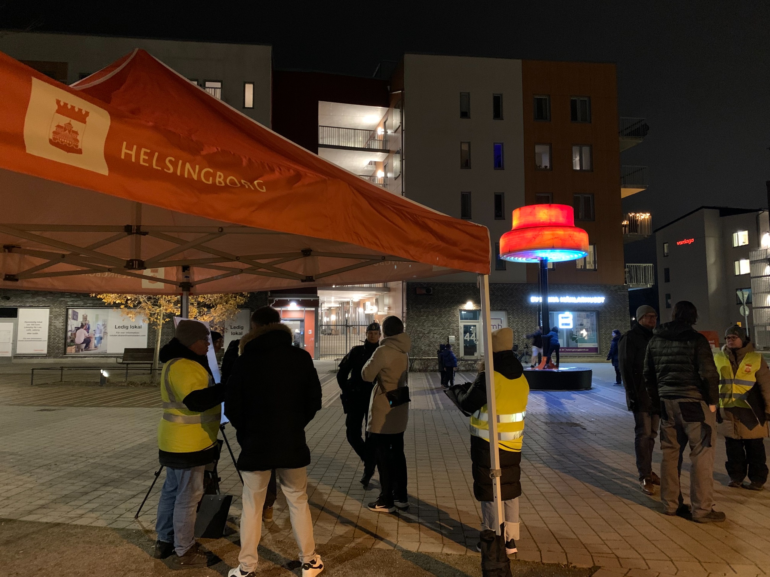 Personer på ett torg framför en stor röd lampa