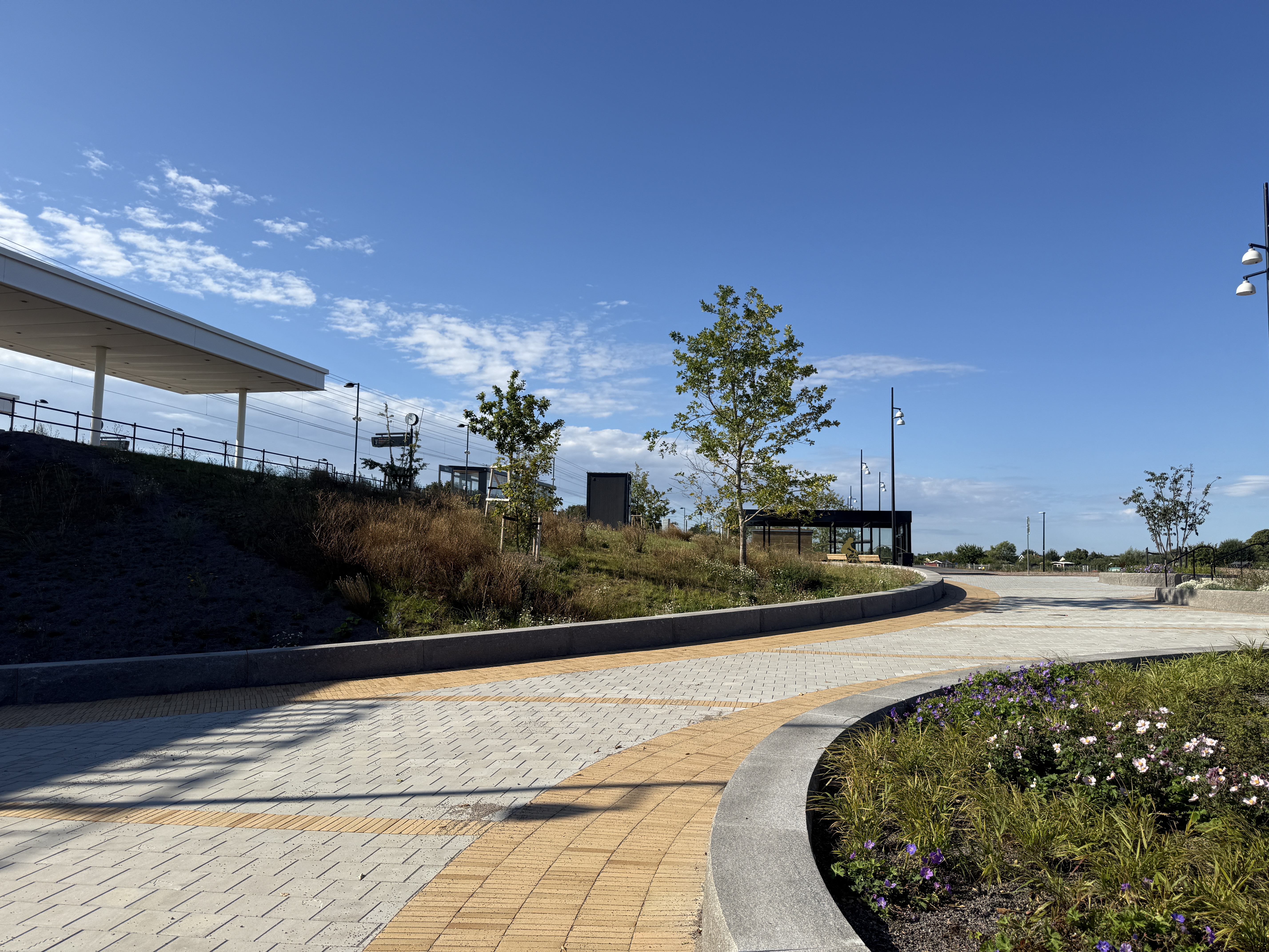 Maria station, plattlagt gångväg, planteringar av träd och blommor.