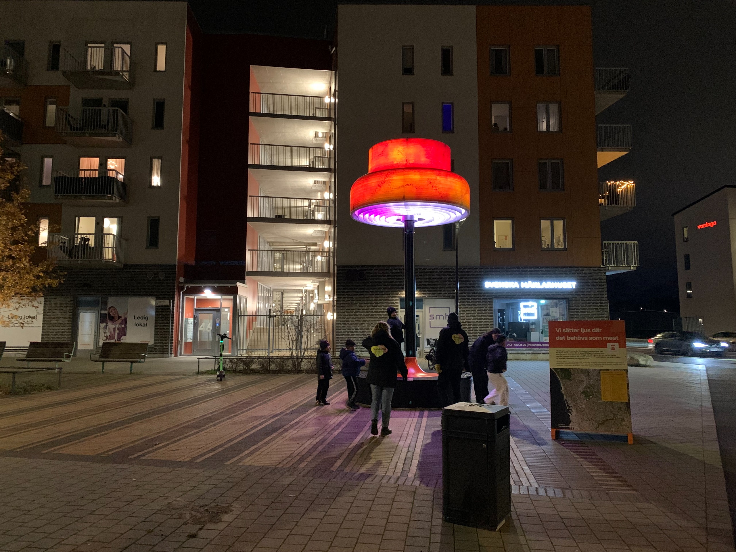 Personer på ett torg framför en stor röd lampa